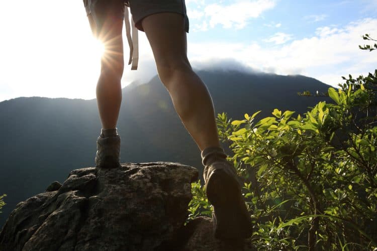 woman hiker legs climbing on sunrise mountain peak rock