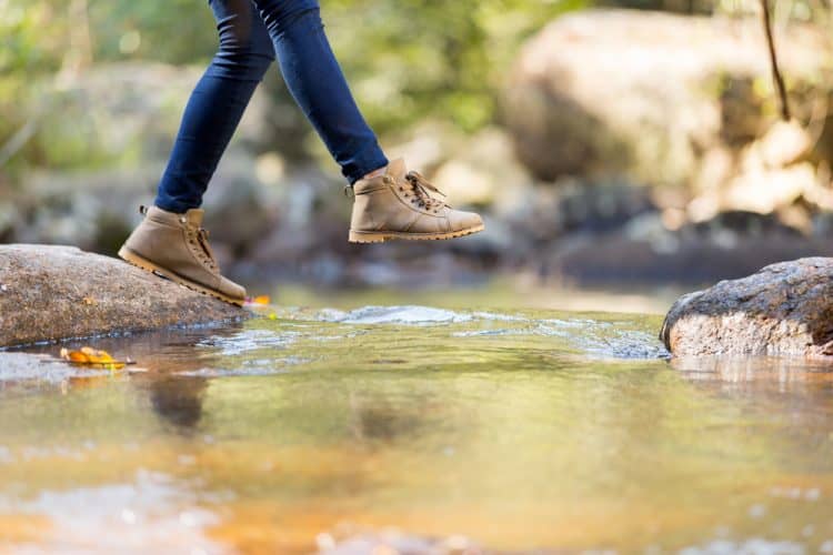 a girl crossing a stream with jeans