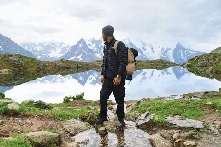 a man sitting next to a lake wearing hiking pants